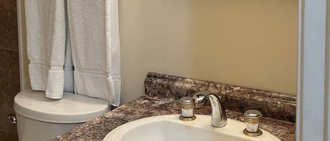 A bathroom with a white sink, a marble countertop, a mirror, and two white towels hanging on a towel rack.