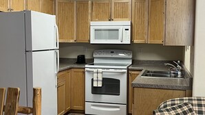 A compact kitchen with wooden cabinets, a white refrigerator, a microwave, a stove, and a sink. - Denali Rainbow Village RV Park and Motel (Denali National Park)