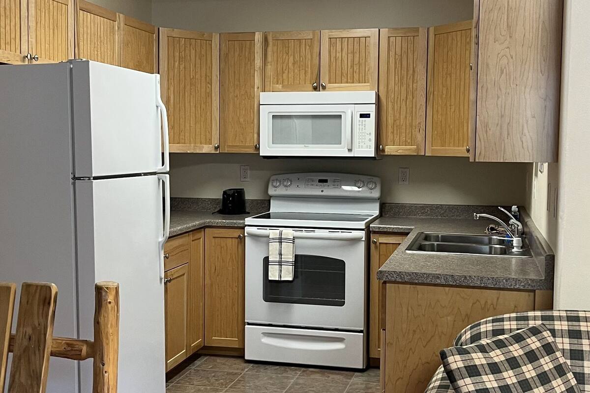 A compact kitchen with wooden cabinets, a white refrigerator, a microwave, a stove, and a sink.