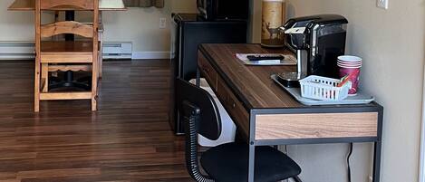 Un espacio habitable compacto con una mesa de comedor de madera, un televisor pequeño, una cafetera y un escritorio con una silla.