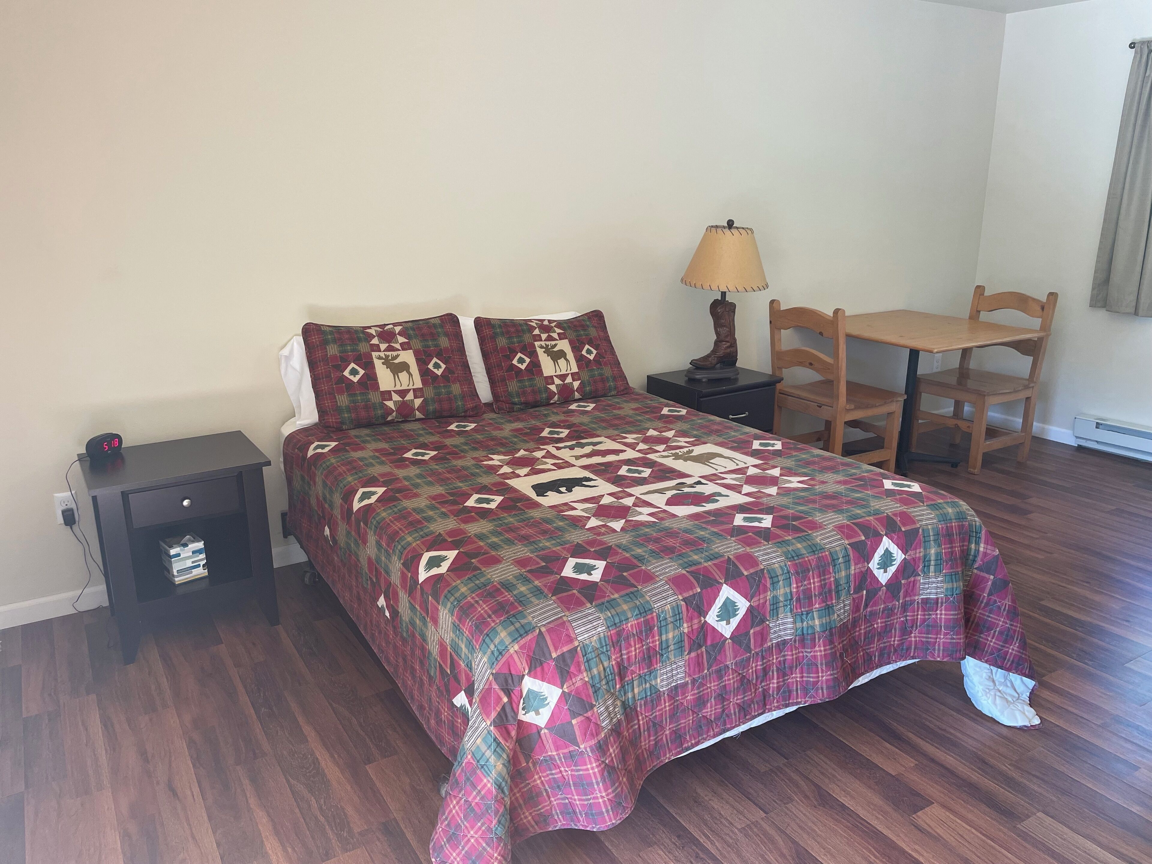 A bedroom with a bed, a nightstand, a lamp, a chair, and a table.