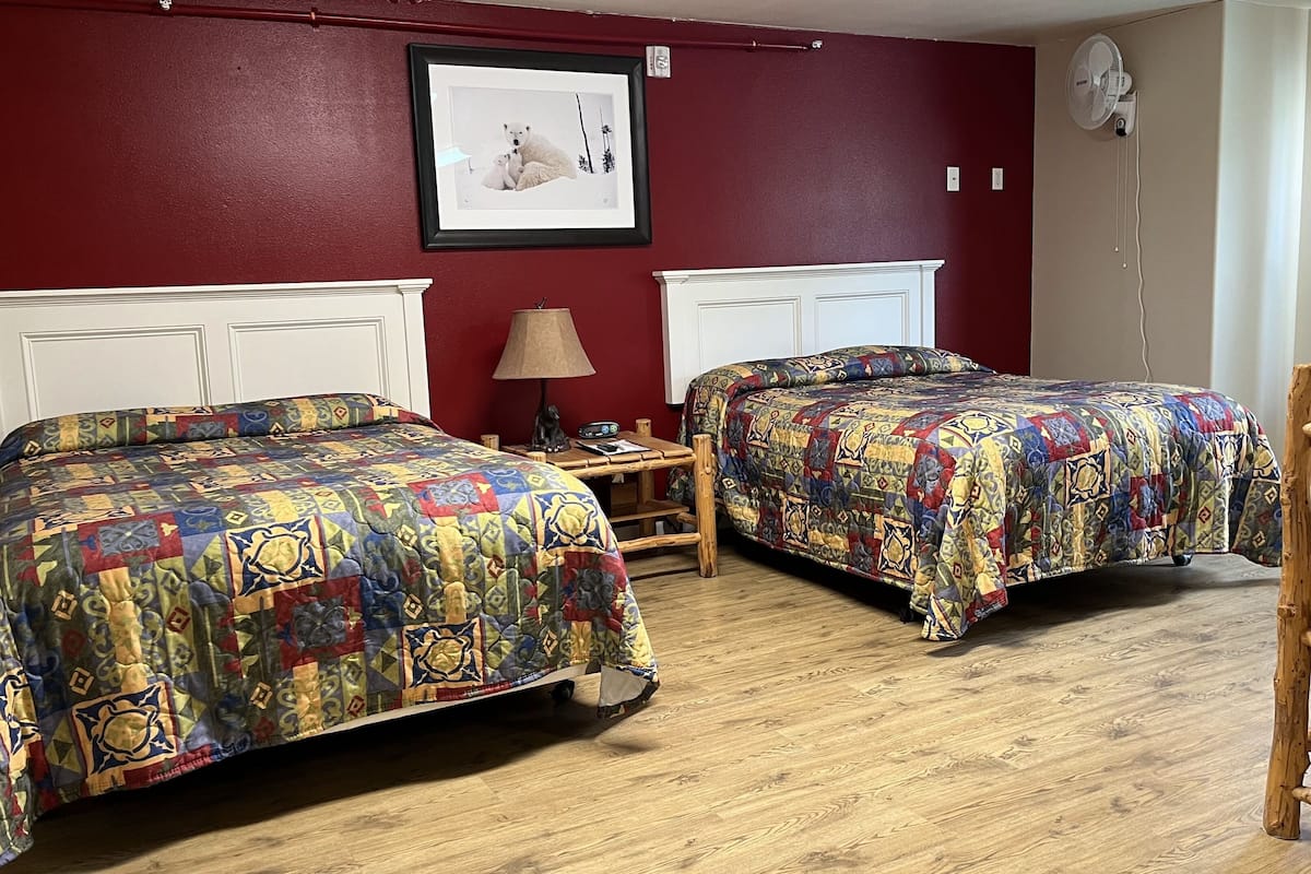 A room with two beds, a wooden chair, a nightstand with a lamp, and a picture on the wall.