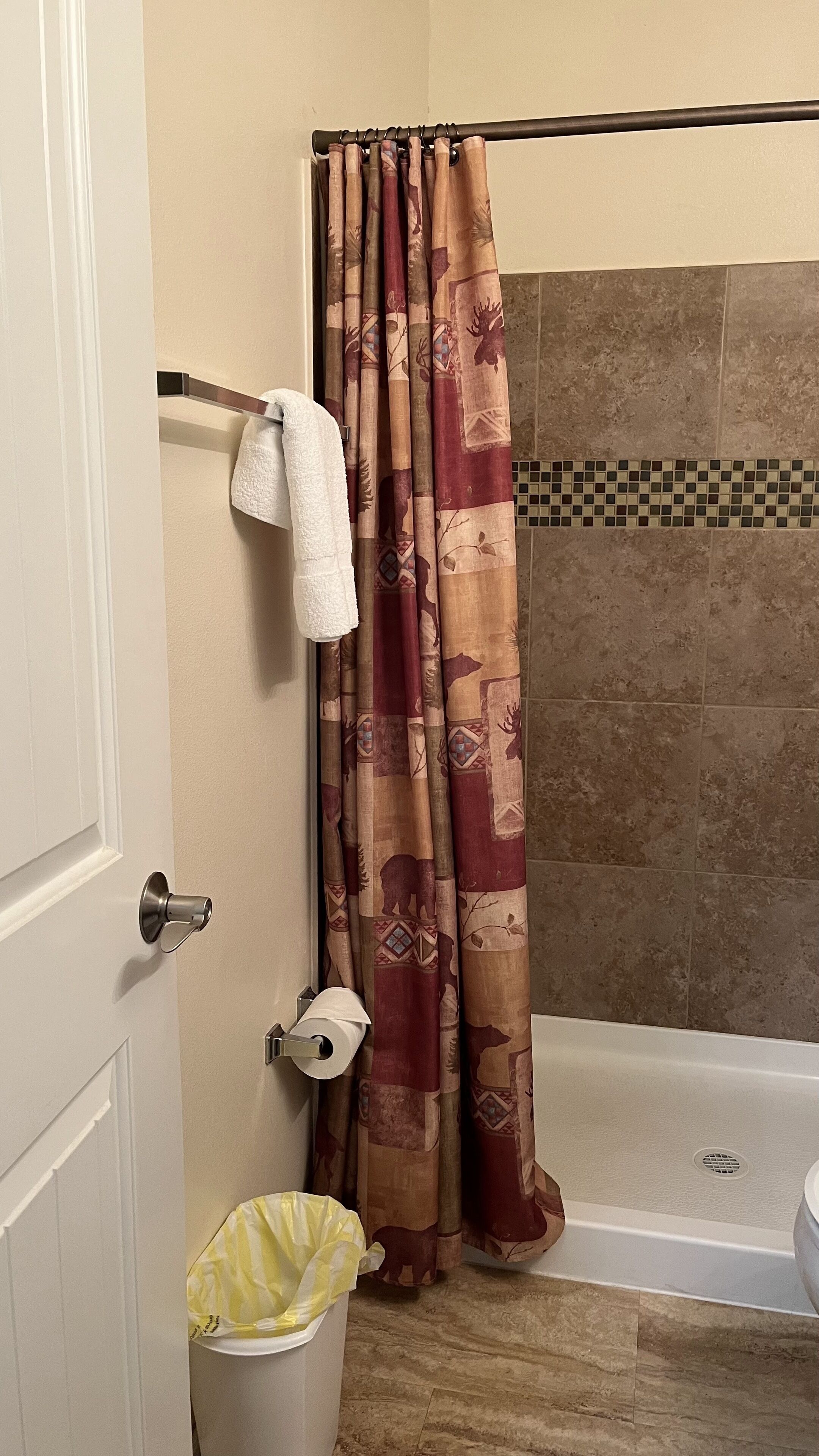 Een badkamer met douchegordijn, handdoekhouder, toiletrolhouder en een prullenbak.