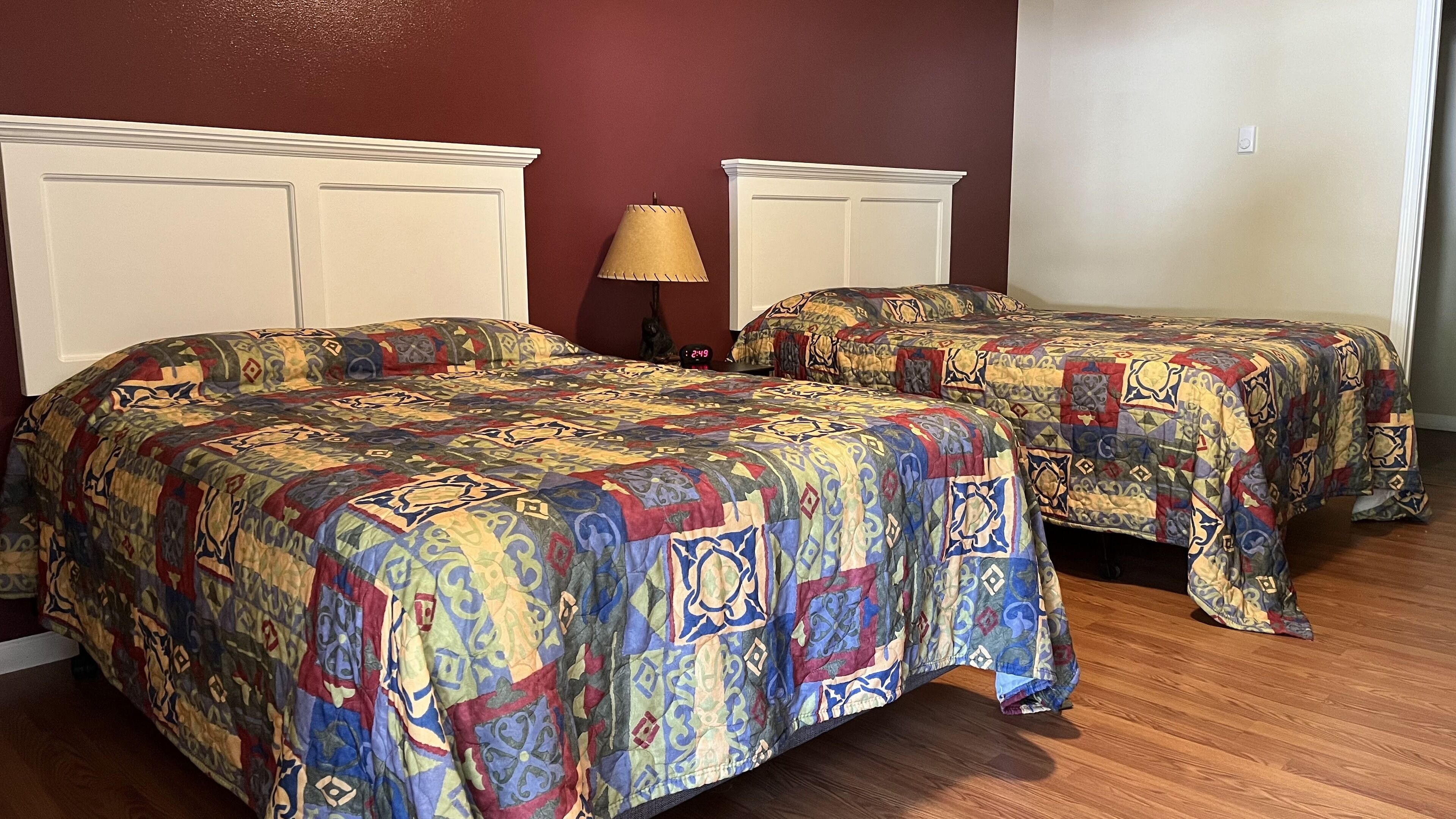 A bedroom with two beds, a nightstand, a lamp, and a wall clock.