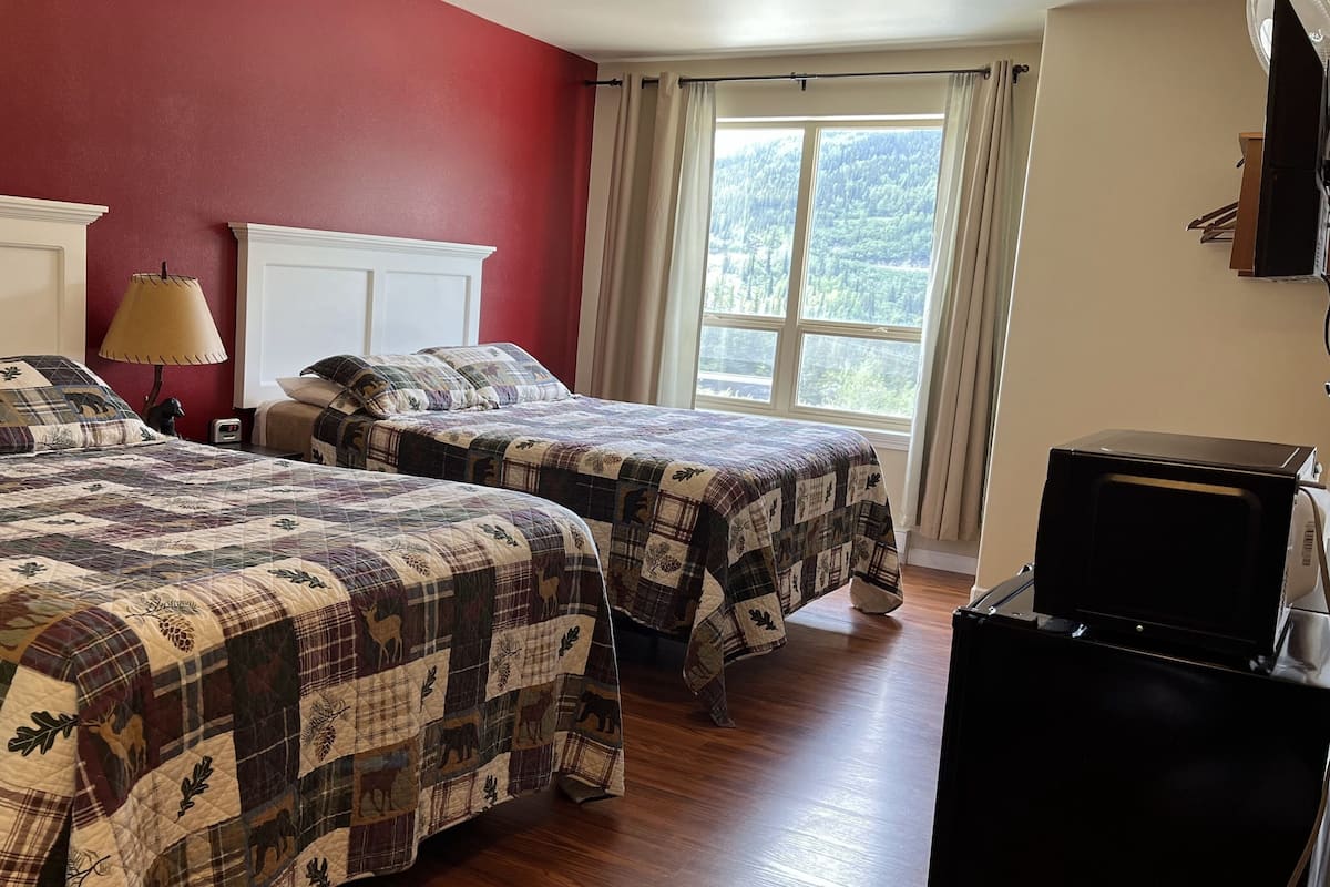 A room with two beds, a lamp, a clock, and a TV.