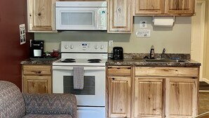 A compact kitchen with wooden cabinets, a microwave, stove, and a sink. - Denali Rainbow Village RV Park and Motel (Denali National Park)