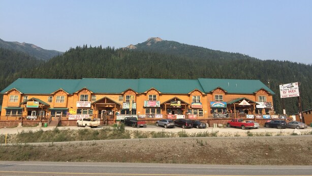 A multi-story building with a green roof, several storefronts, and a sign indicating a Rainbow Village RV Park and Motel. - Denali Rainbow Village RV Park and Motel (Denali National Park)