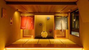 Una habitación japonesa tradicional con suelo de tatami, puertas correderas y un jarrón decorativo en el centro.