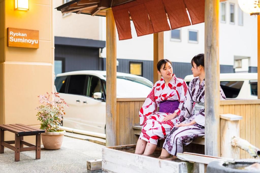 A wooden bench and a potted plant outside a building with a sign reading 'Ryokan Suminoyu'.