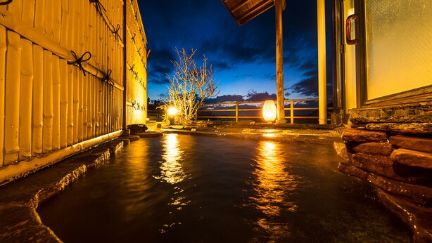 Un onsen japonés tradicional con un vestuario de madera, escalones de piedra que conducen al agua y vistas del cielo al atardecer.