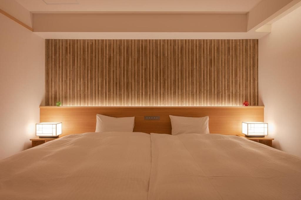 Une chambre d’hôtel avec un grand lit, une tête de lit en bois, des lampes de chevet et un luminaire fixé au mur.