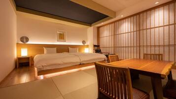 Una habitación de hotel con cama, mesita de noche, lámpara y una mesa de comedor con sillas.