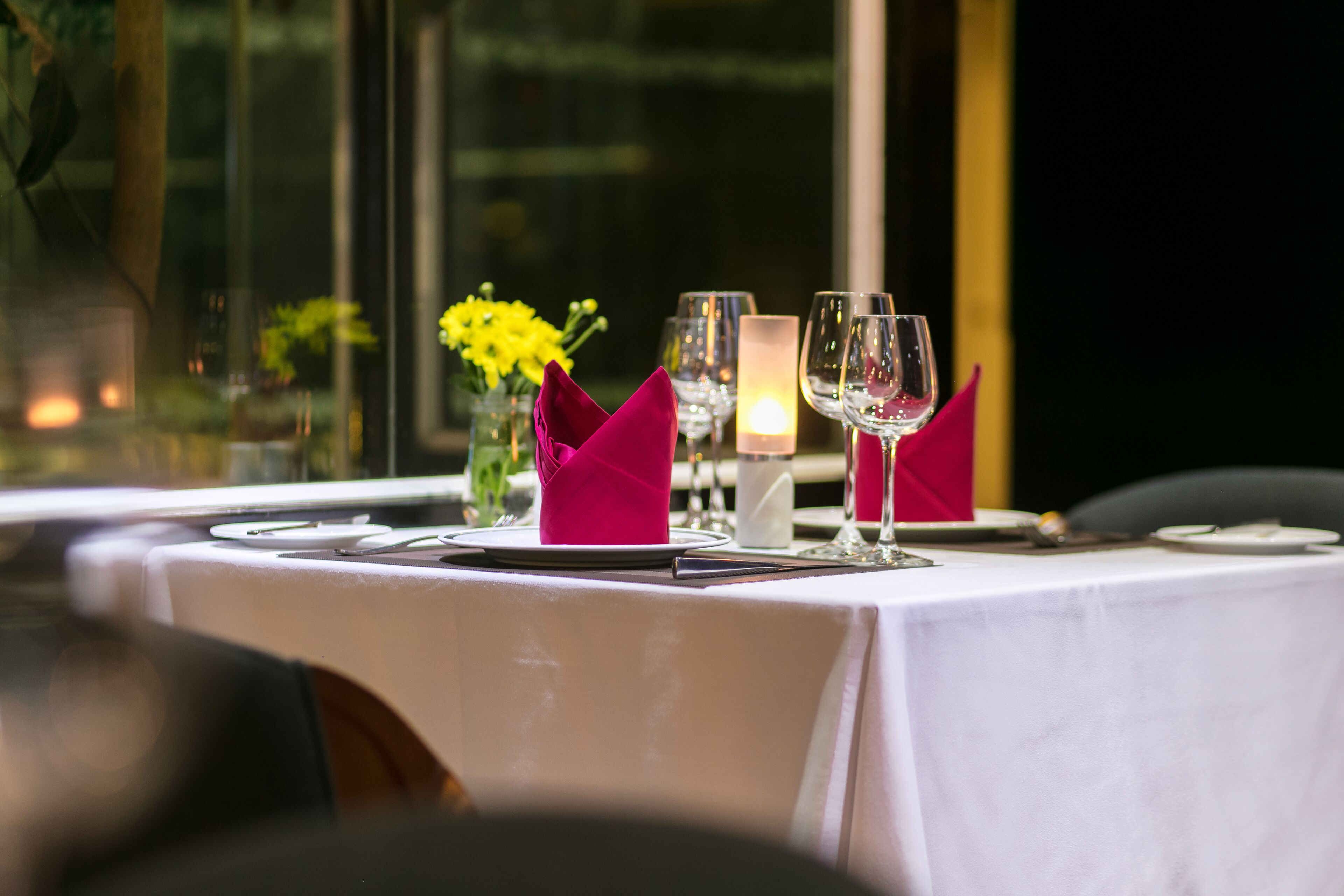 A table set for dining with a candle, glasses, and a vase of yellow flowers.