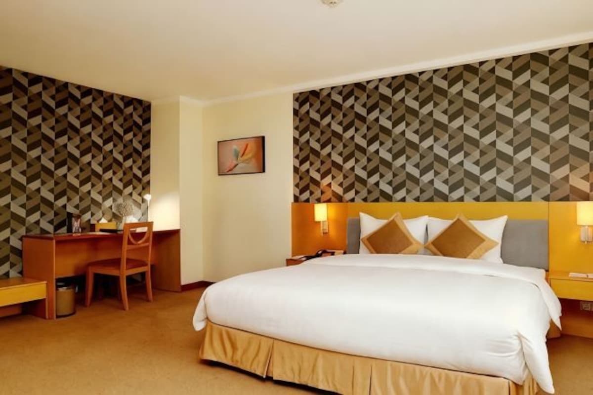 Une chambre d’hôtel avec un grand lit, un bureau avec une chaise, une table de chevet et un mur orné d’un motif géométrique.
