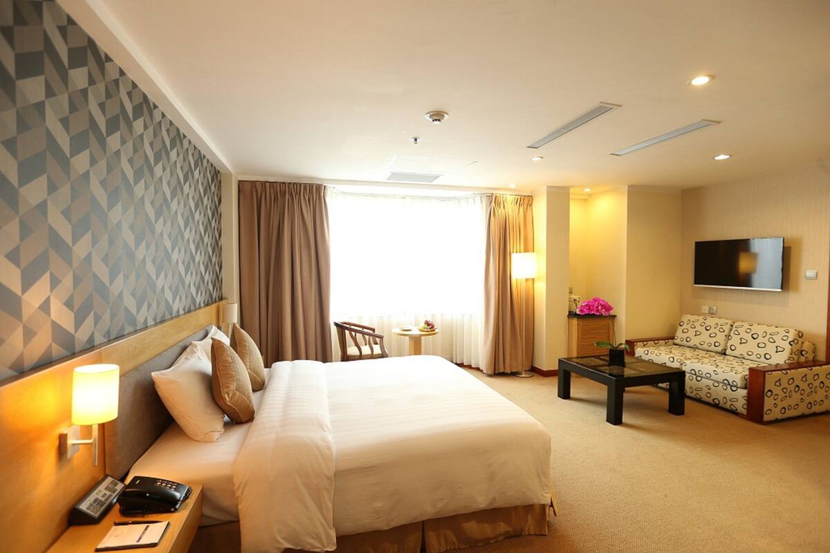Habitación de hotel con una cama grande, un sofá, una mesita, un televisor y una ventana con cortinas.