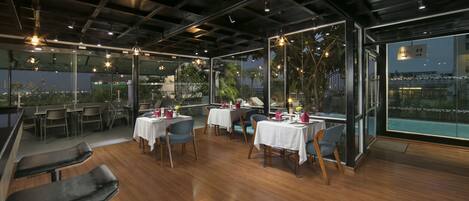 Un restaurante moderno con suelo de madera, paredes de vidrio y mesas dispuestas para comer.
