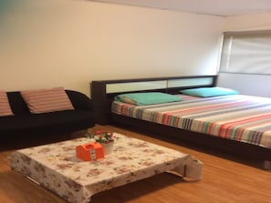 A small, furnished room with a bed, a sofa, and a table with a floral tablecloth.