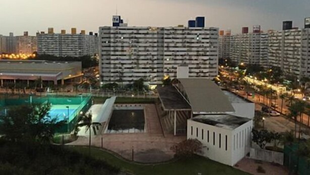 Un edificio residencial alto con piscina en la azotea y cancha deportiva cubierta.