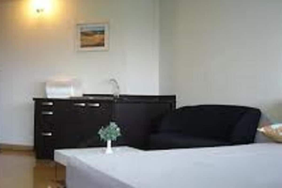 A hotel room with a bed, a small table, a dresser, and a refrigerator.