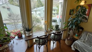 A cozy room with a wooden table, two chairs, a sofa, and large windows offering a view of the neighborhood. - Bellscabin Guesthouse (Karuizawa)