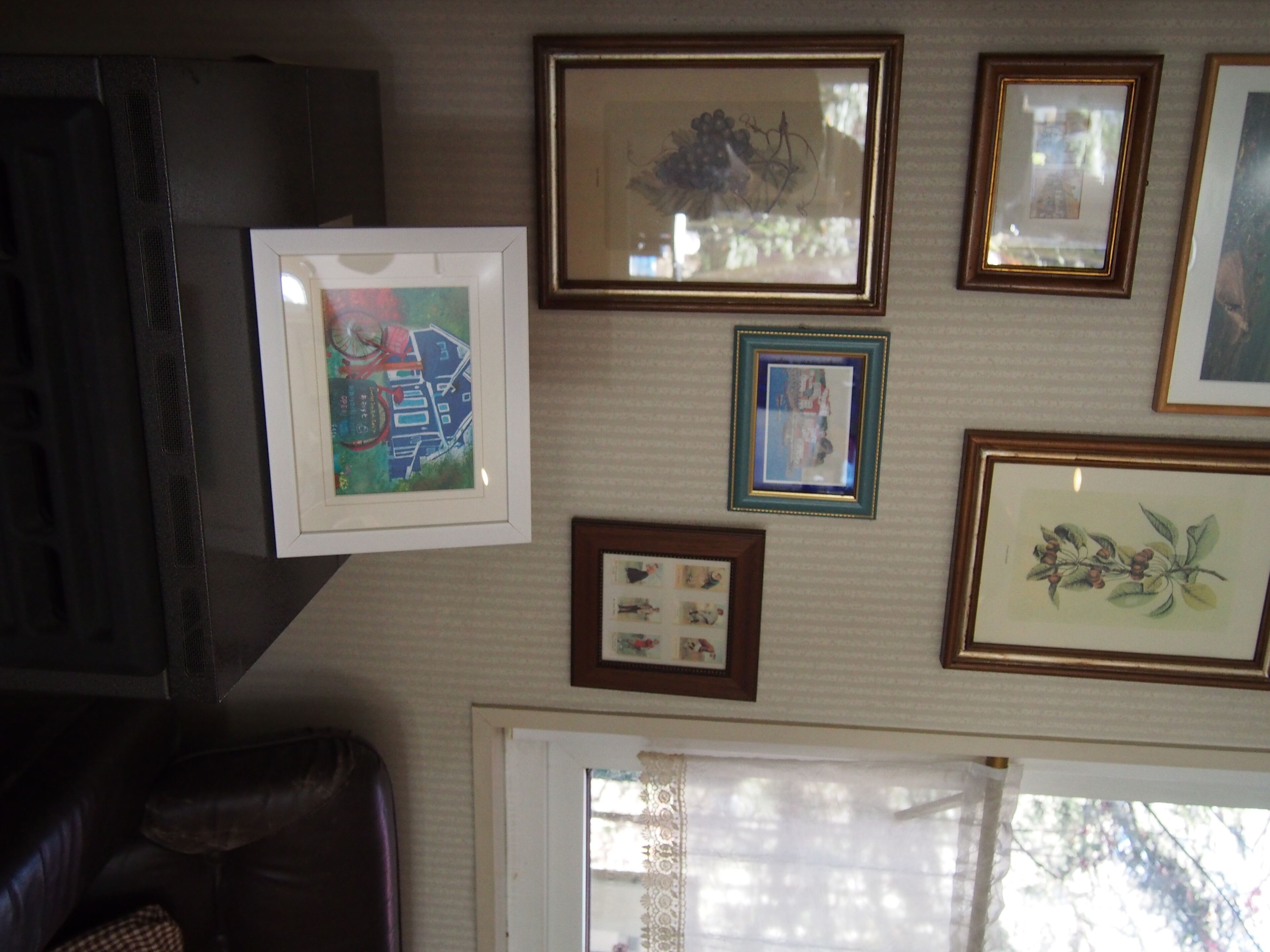 A room with a brown leather sofa, a framed picture of a bicycle, and a window with a lace curtain.