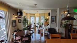 A spacious living area with a wooden dining table, several chairs, a sofa, and a coffee table. There are multiple potted plants and hanging lamps. - Bellscabin Guesthouse (Karuizawa)