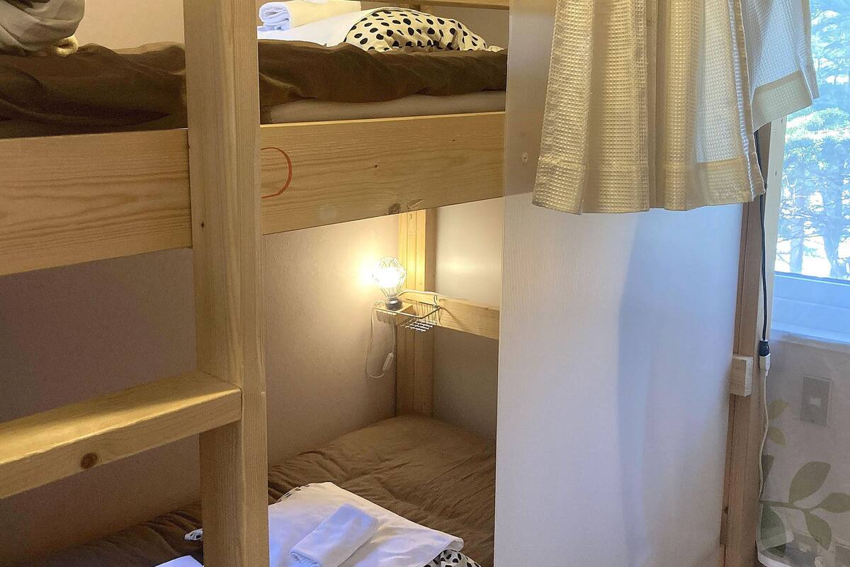 A bunk bed room with a window, a bedside lamp, and a curtain.