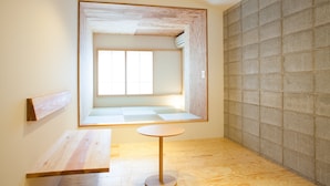 A minimalist room with a wooden floor, a round table, a bench, and a large window.