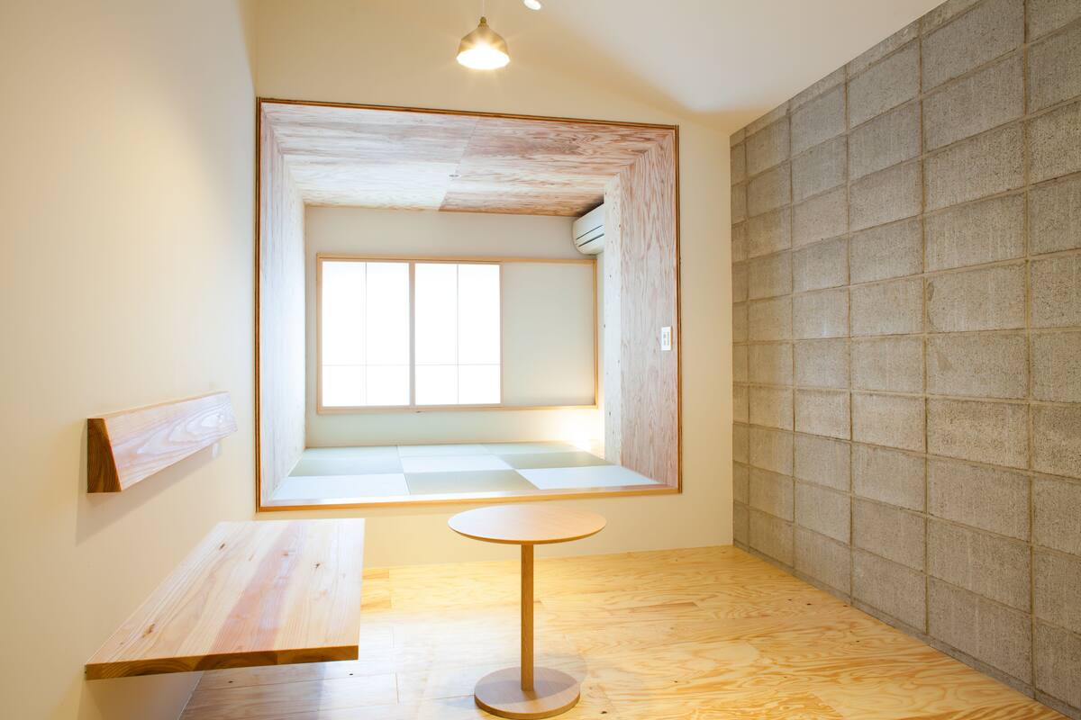 Une pièce au décor minimaliste, avec un plancher en bois, une table ronde, un banc et une grande fenêtre.