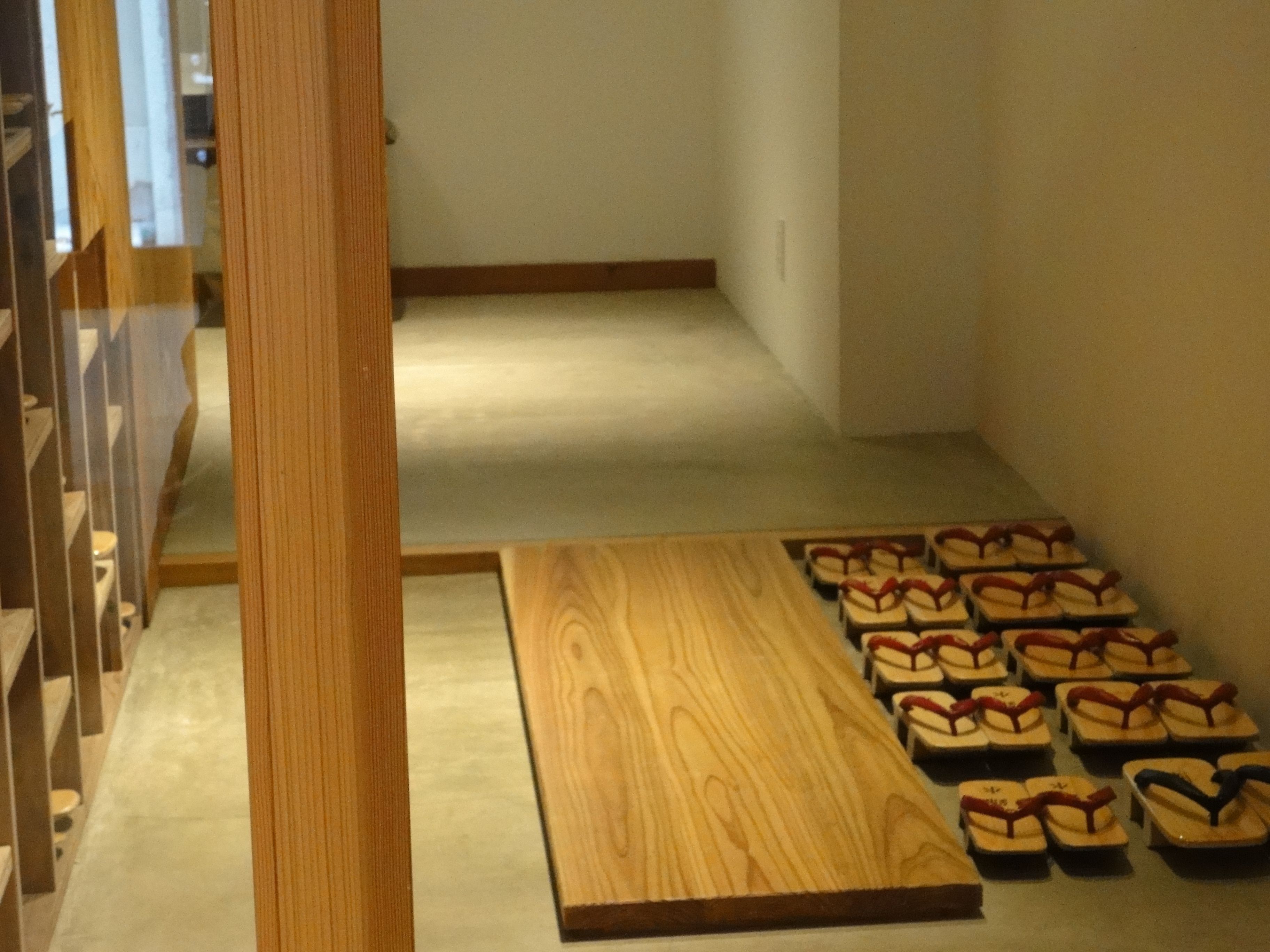 A hallway with a wooden floor and a row of flip-flops lined up against the wall.
