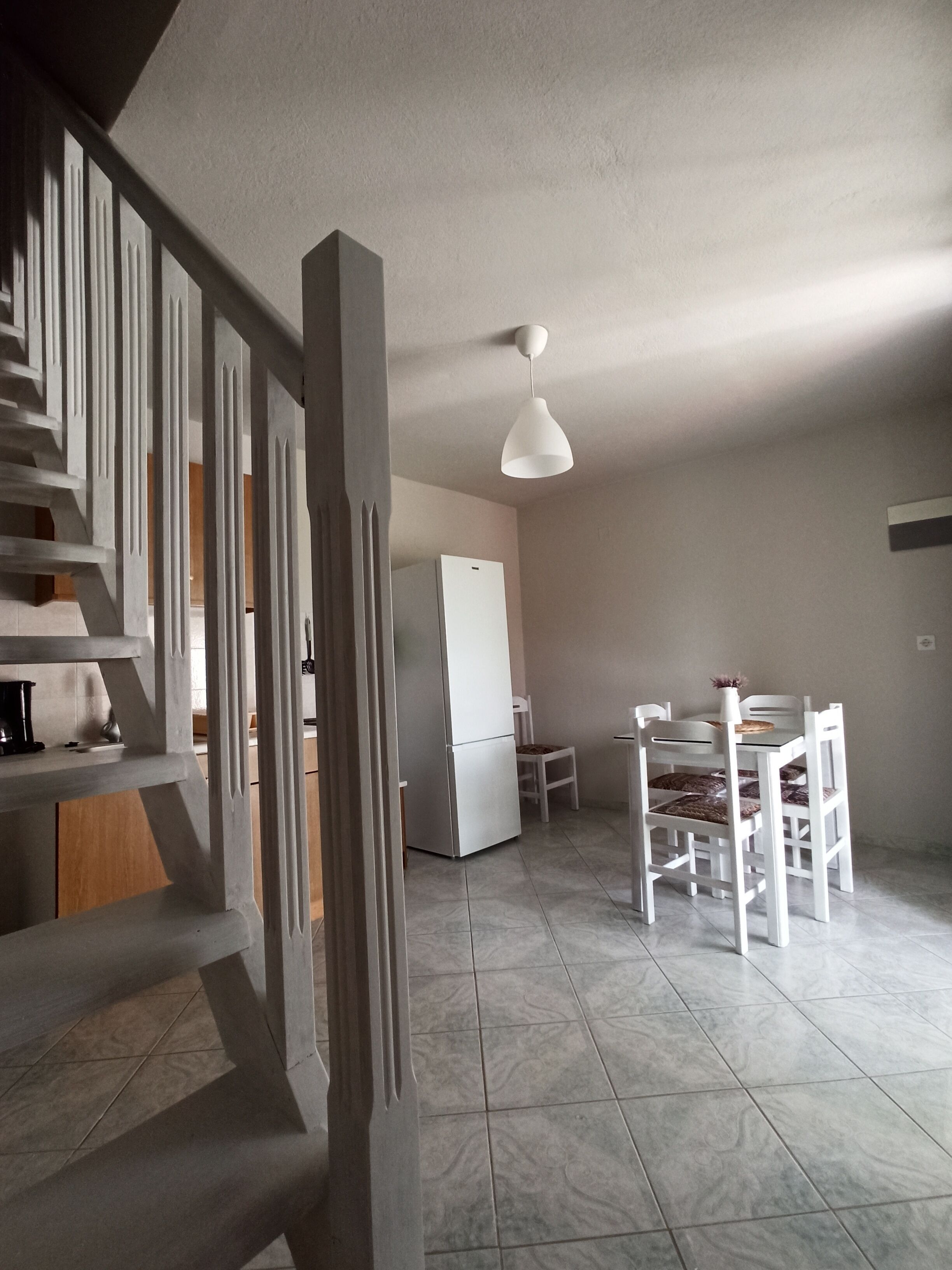 Una cocina amplia con un refrigerador blanco, una mesa de comedor con sillas y una lámpara colgante moderna.