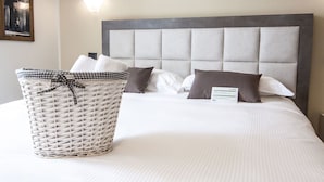 A neatly made bed with a grey upholstered headboard, a wicker basket with a checkered ribbon, and a wall-mounted light fixture. - Hotel Le Vigne di Corvino (Corvino San Quirico)