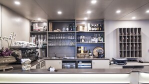 A modern bar area with shelves of liquor bottles, glasses, and a coffee machine. - Hotel Le Vigne di Corvino (Corvino San Quirico)