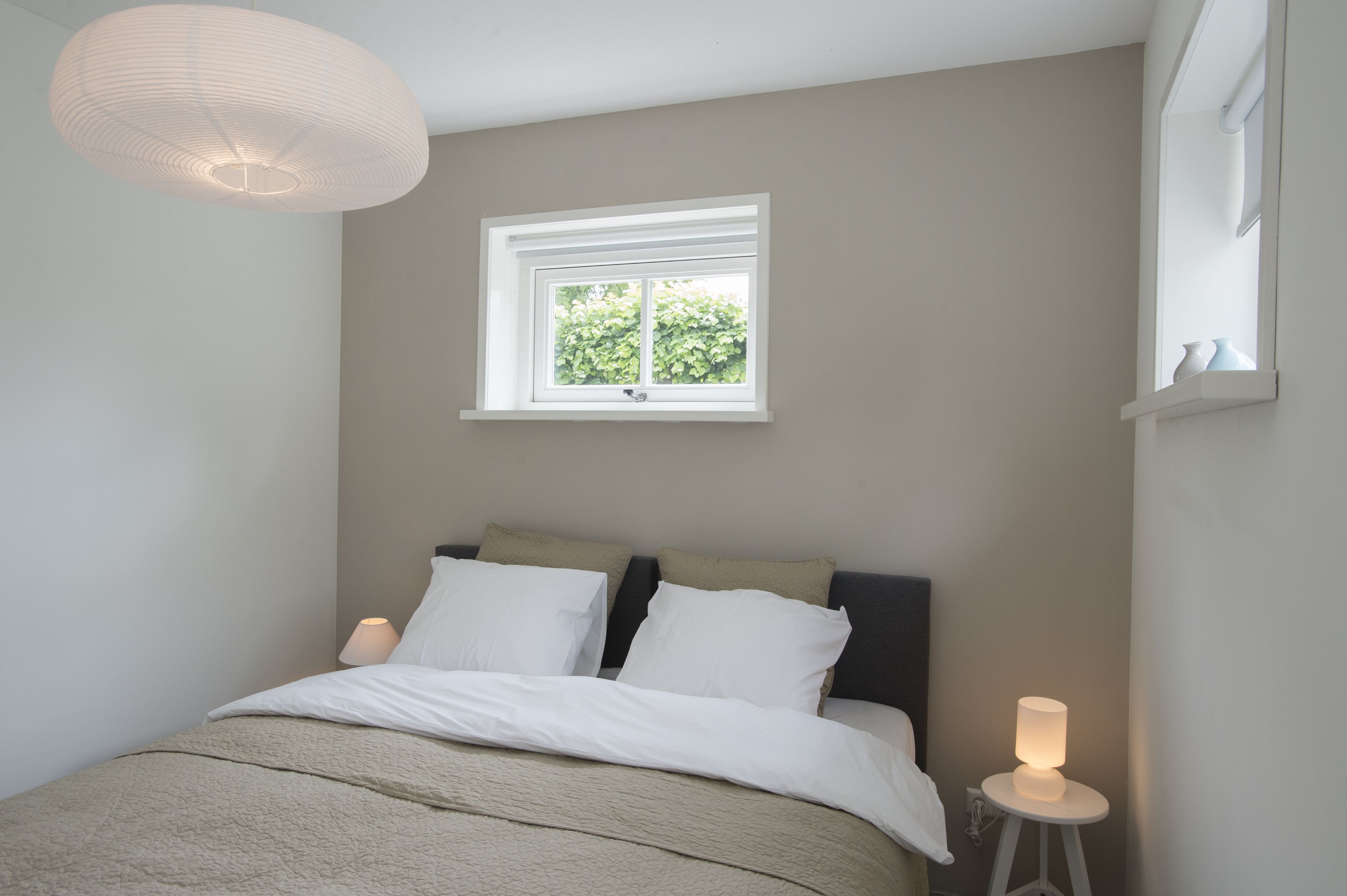 A bedroom with a bed, bedside lamps, a window, and a hanging light fixture.