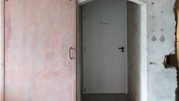 Una stanza con una porta rosa, una porta bianca e un muro in cemento con evidenti danni.