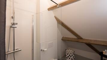Un baño moderno con cabina de ducha de vidrio, una viga de techo de madera y un inodoro blanco.