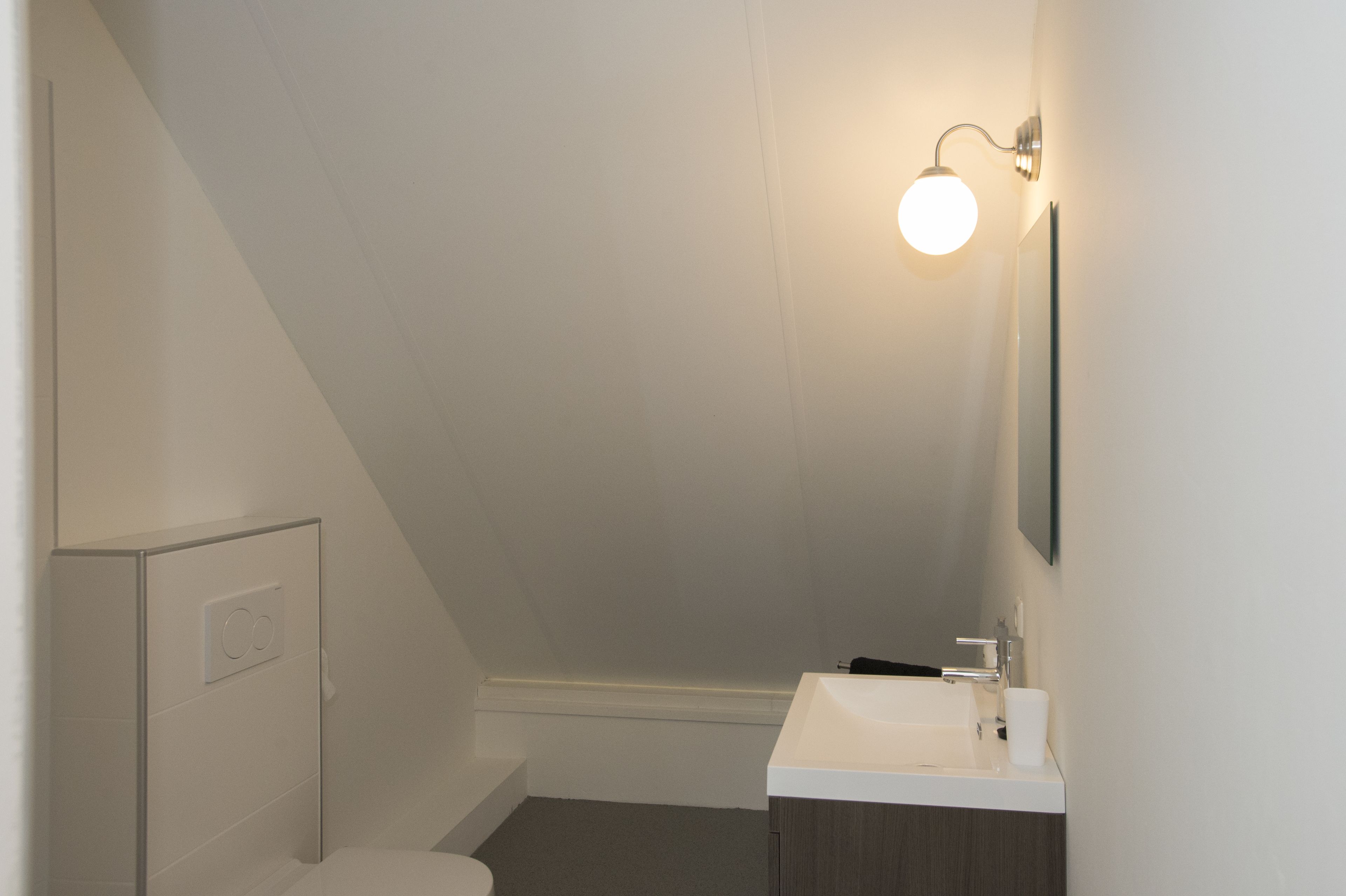 Un baño pequeño y moderno con un lavabo blanco, un espejo y una lámpara.