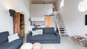 A modern living room with a grey sofa, a wooden cabinet, a staircase, and a kitchen area.