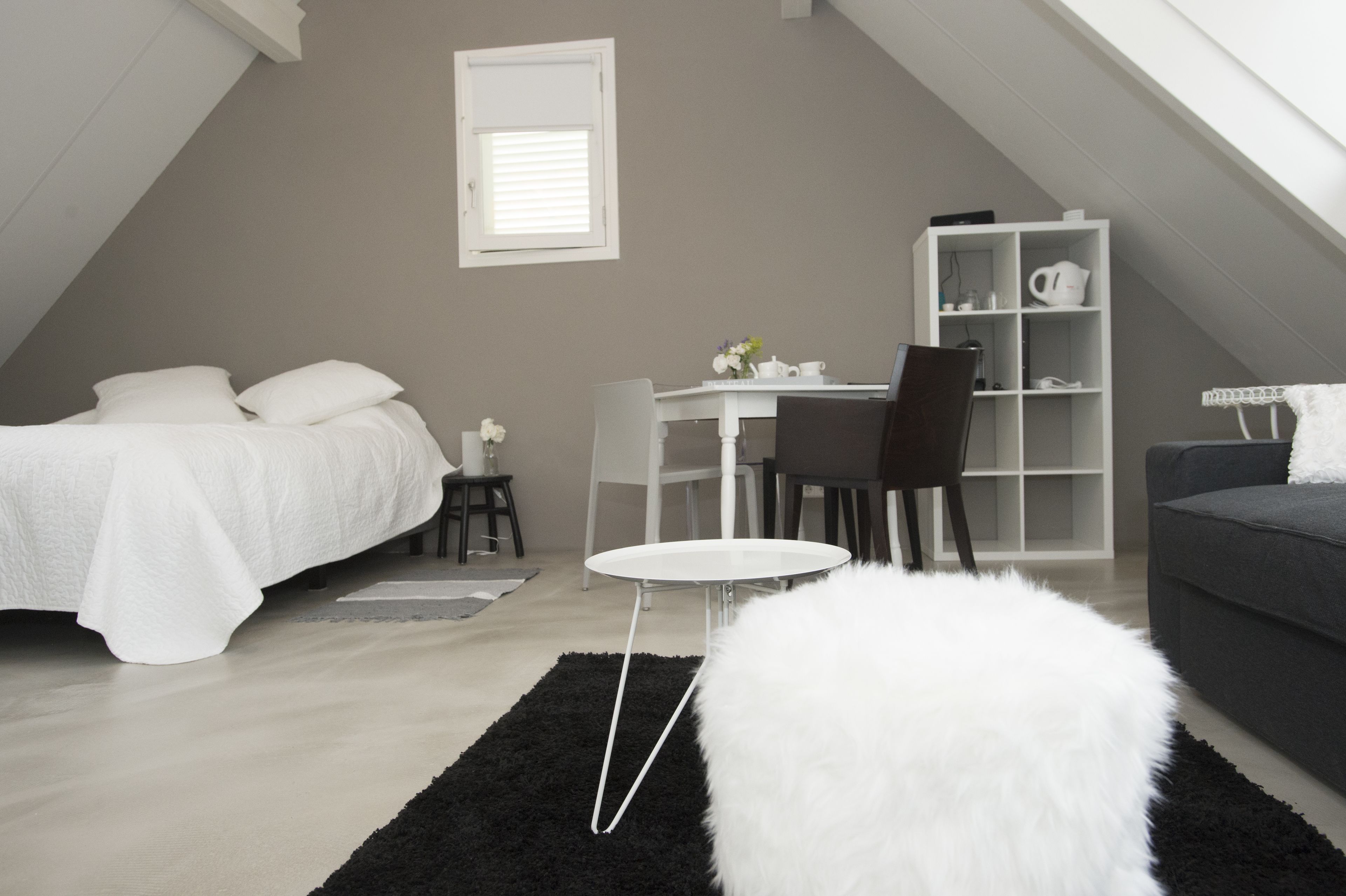A modern bedroom with a bed, a desk, a chair, a small table, a bookshelf, and a sofa.