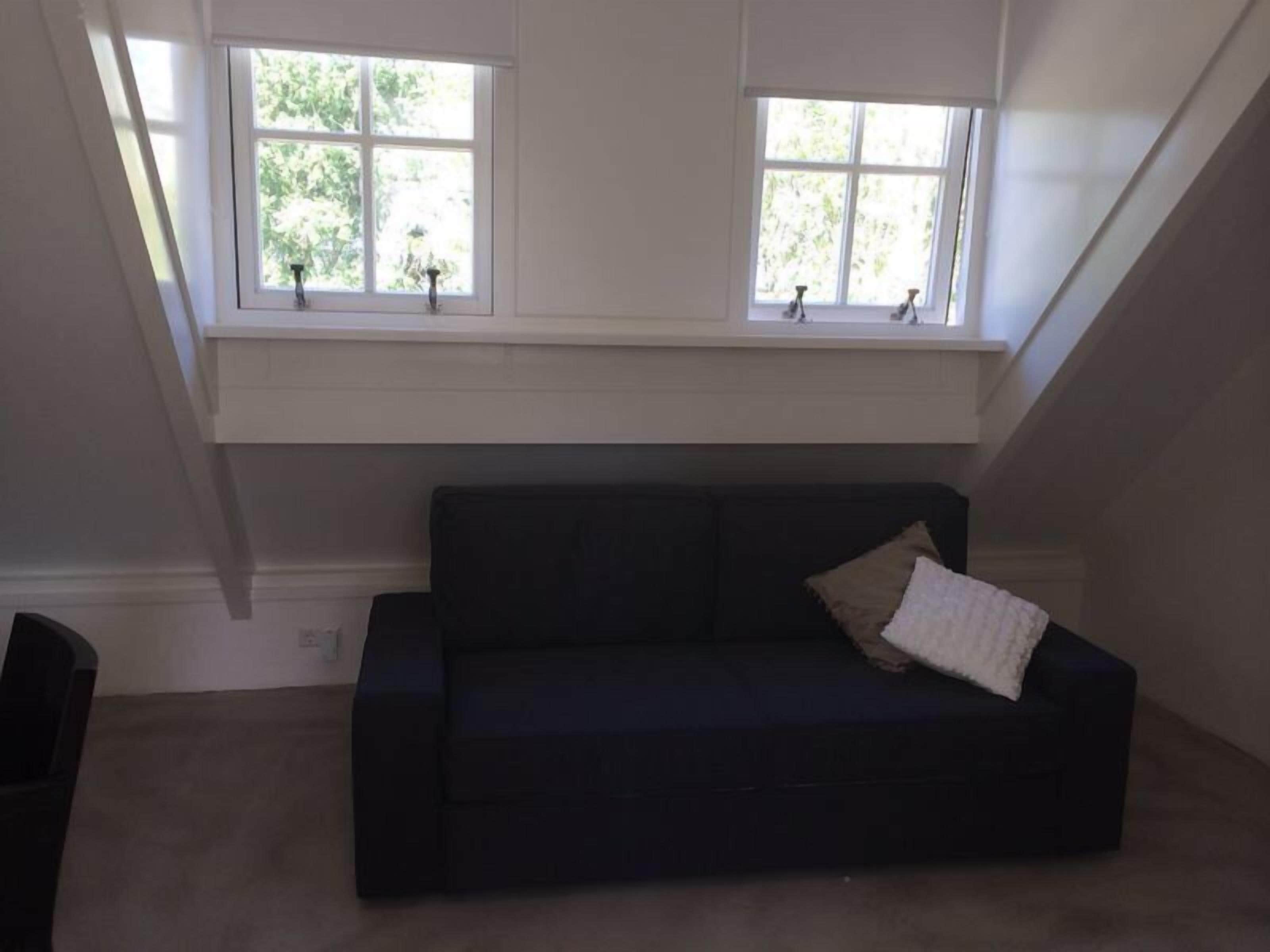 A dark-colored sofa with a cushion and a window above it.