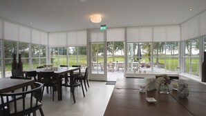 A spacious room with large windows, a wooden table, and chairs.