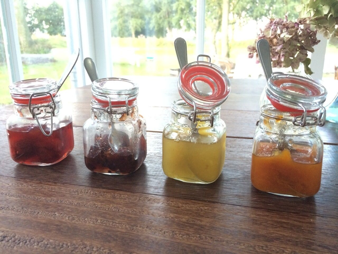 Quatre bocaux en verre avec des couvercles et des cuillères en métal, posés sur une table en bois.