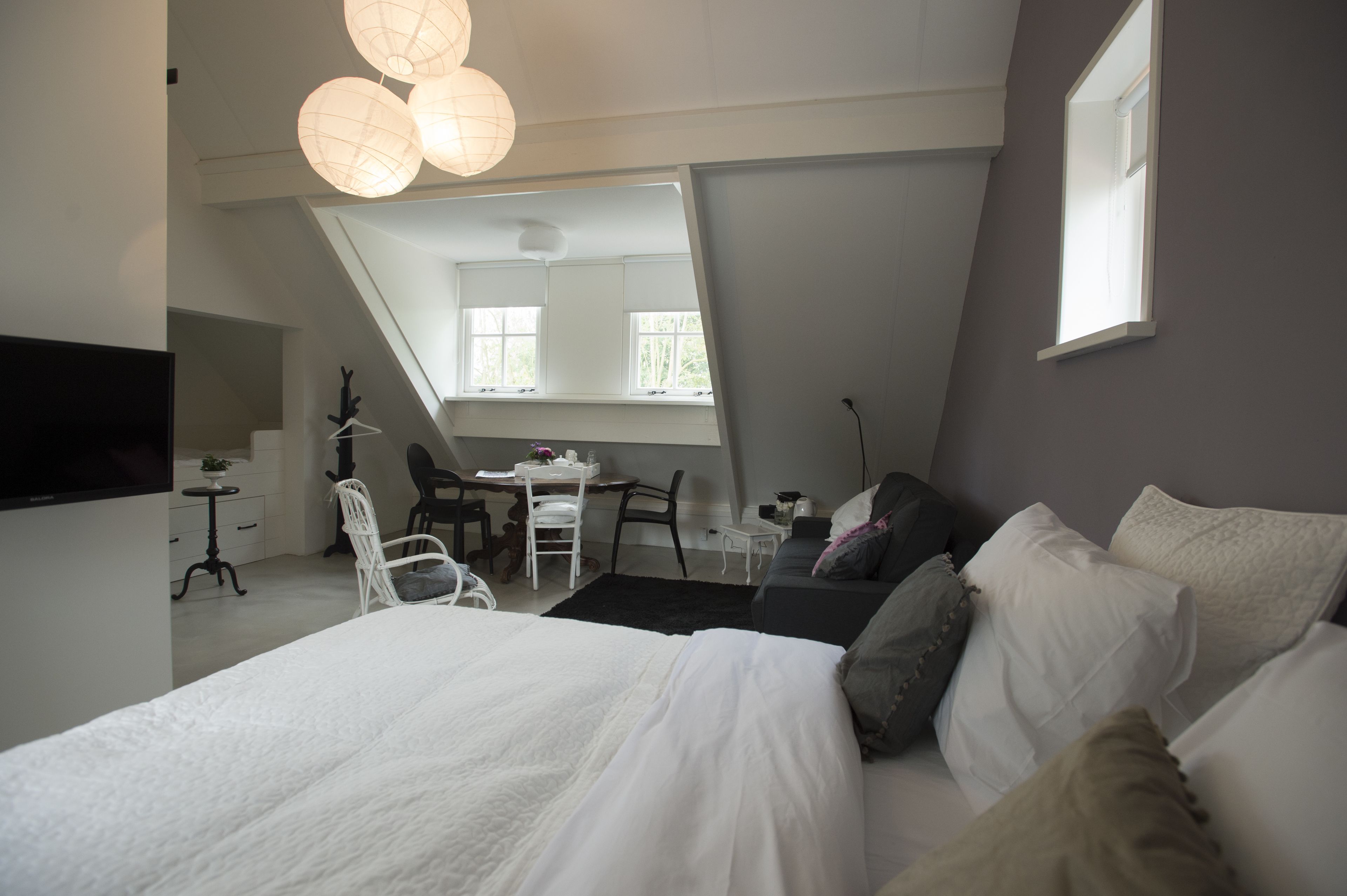 Ein Schlafzimmer mit einem großen Bett, einem Schreibtisch und einem Stuhl. Es gibt ein Fenster und einen an der Wand befestigten Fernseher.
