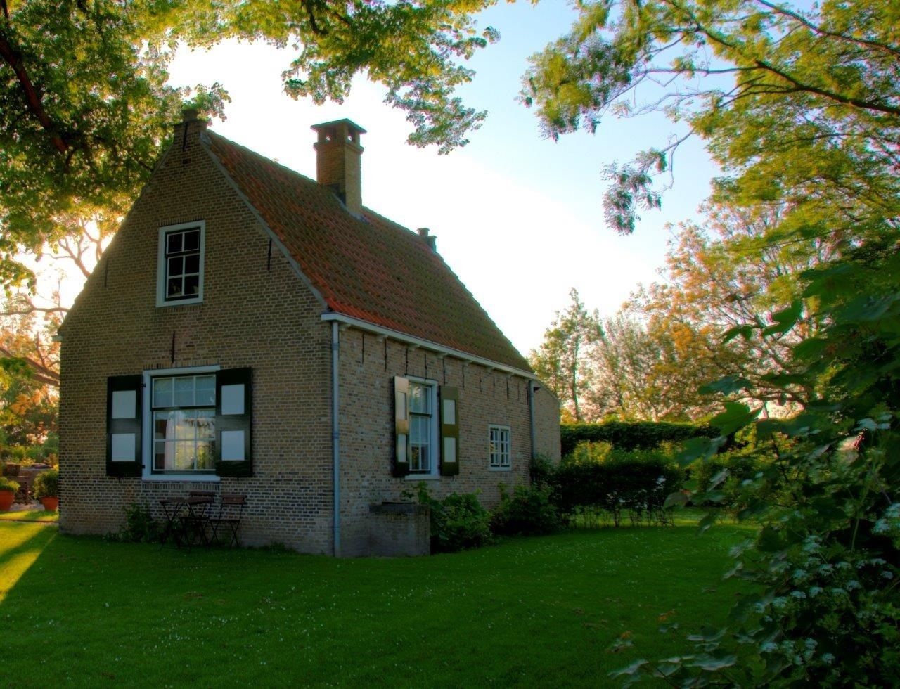 A brick house with a sloped roof and a chimney, surrounded by a well-maintained lawn and trees.