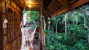 Interior de madera con una hamaca, paneles de madera y vista a un bosque verde y frondoso.