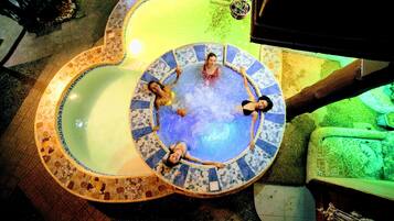 Un jacuzzi circular con mosaicos, rodeado de un suelo de baldosas y un sofá verde.