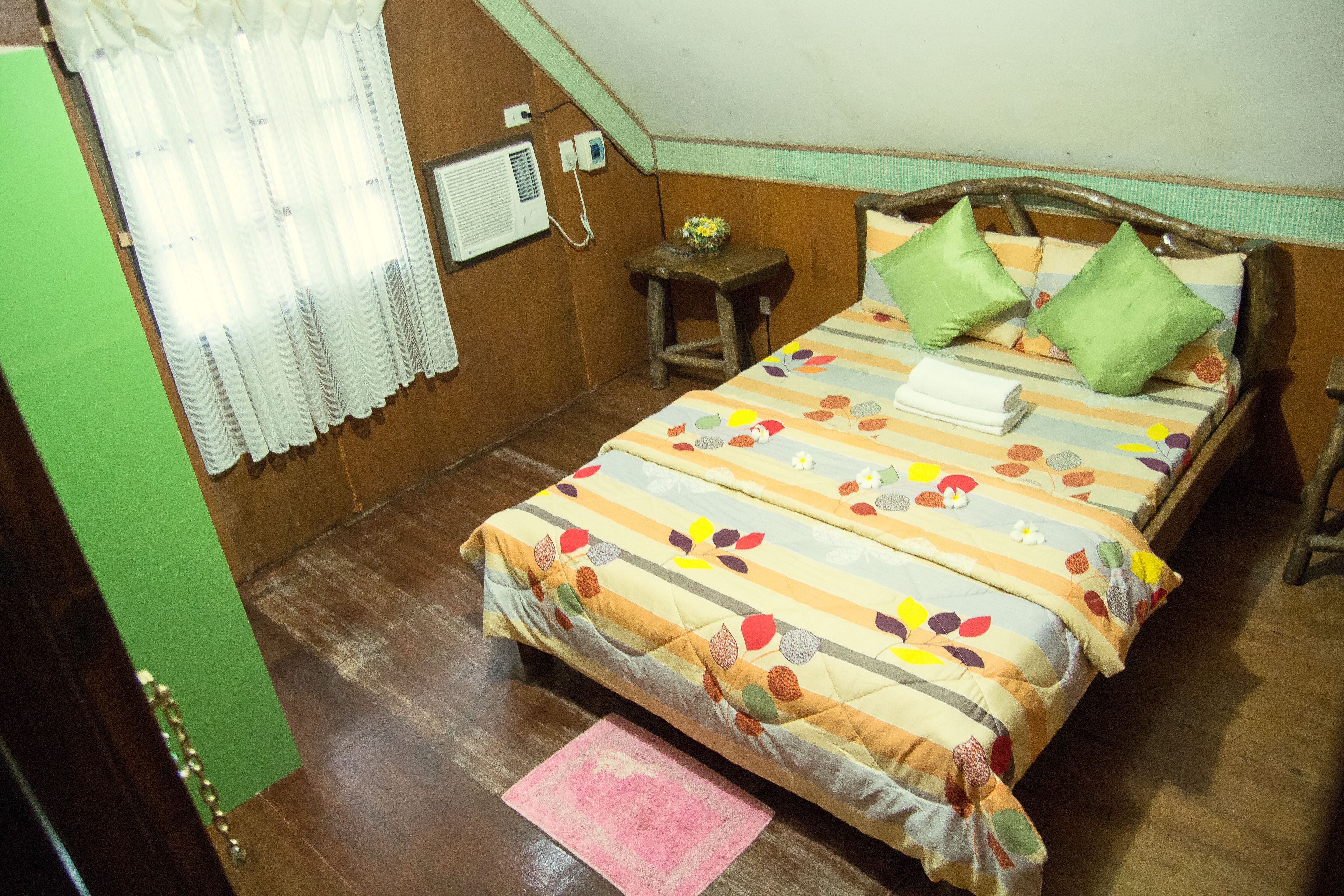 A bedroom with a bed, pillows, a small table, and a wall-mounted air conditioner.