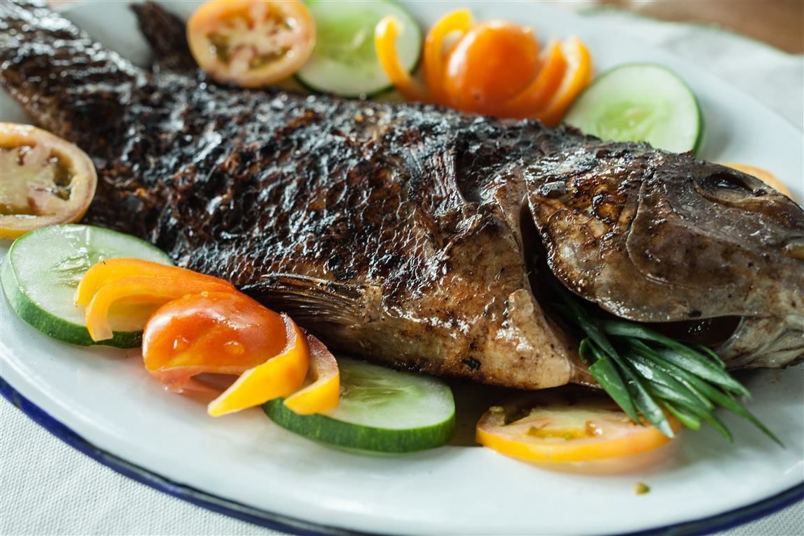 Un pescado entero a la parrilla con rodajas de tomate y pepino en un plato.