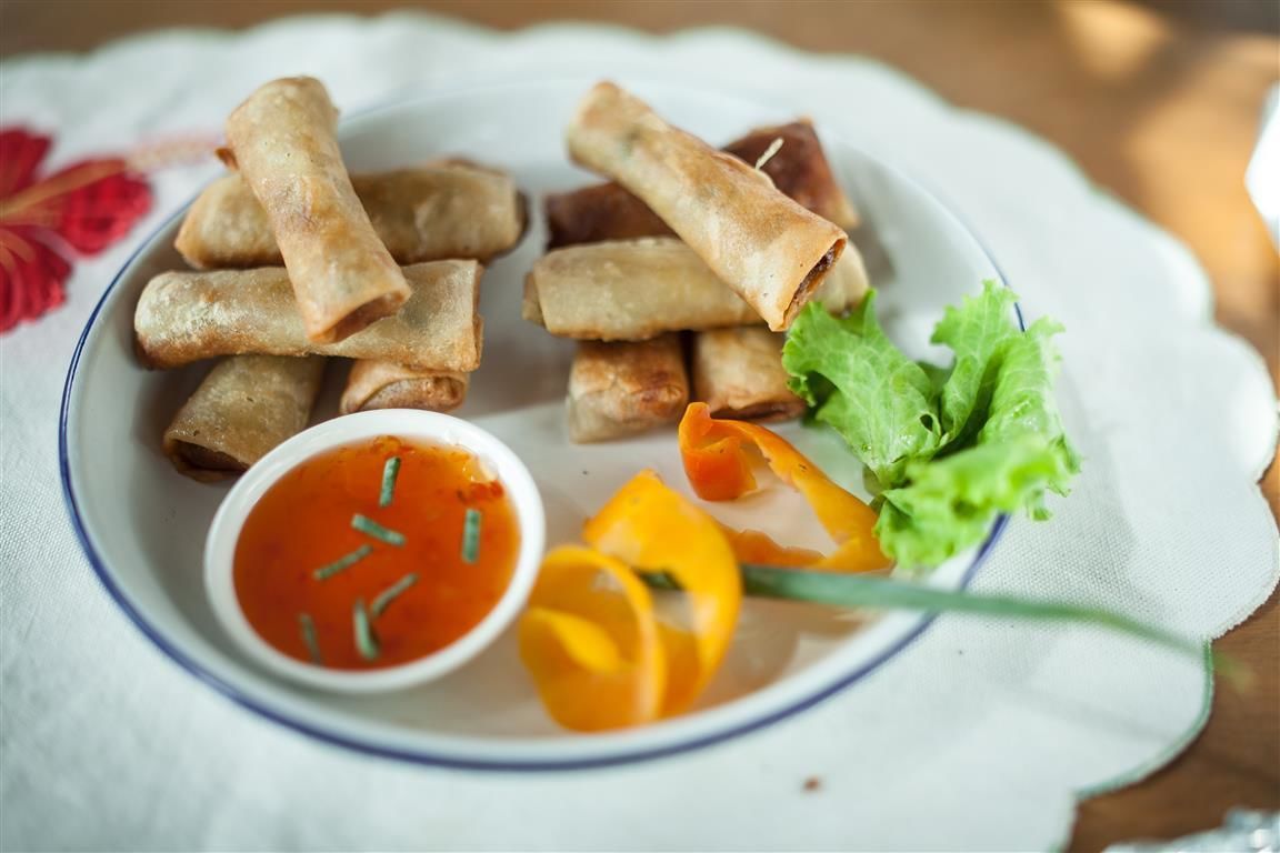 A plate of spring rolls with a dipping sauce and fresh vegetables.