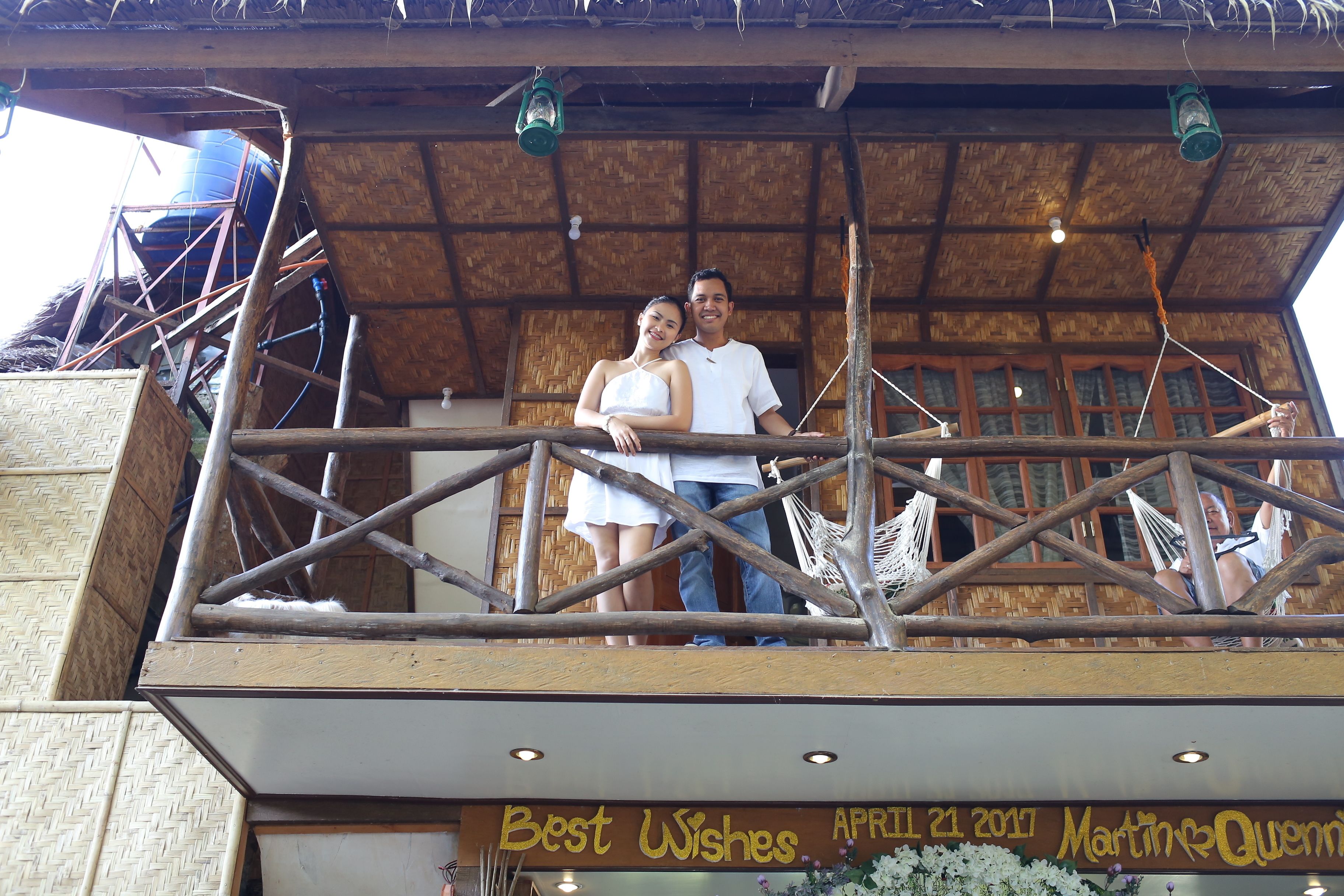A wooden balcony with a thatched roof, a hammock, and a sign reading "Best Wishes April 21, 2017 Martin & Quinn."